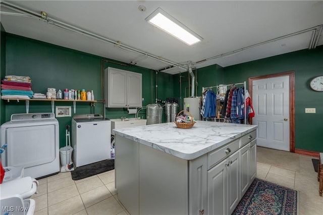 clothes washing area featuring water heater, washer and clothes dryer, light tile patterned floors, and sink