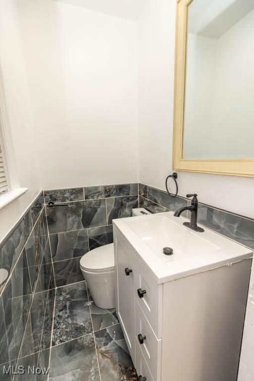 bathroom featuring vanity, toilet, and tile walls