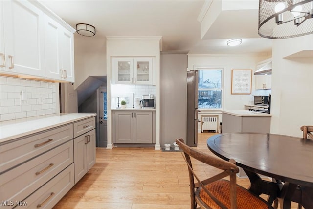 kitchen with white cabinets, tasteful backsplash, radiator, and light hardwood / wood-style floors