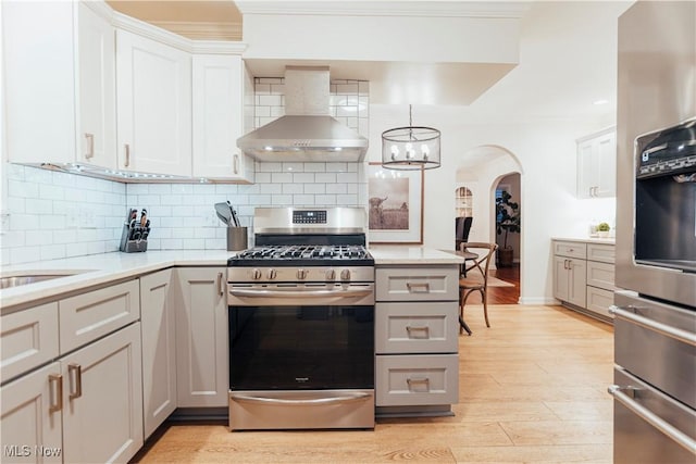 kitchen featuring backsplash, white cabinets, wall chimney range hood, decorative light fixtures, and gas stove