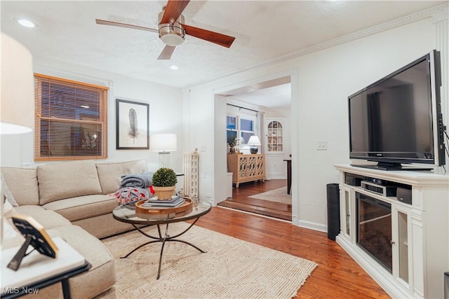 living room with ceiling fan, hardwood / wood-style floors, a textured ceiling, and ornamental molding