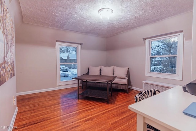 bedroom with radiator heating unit, a textured ceiling, hardwood / wood-style flooring, and multiple windows