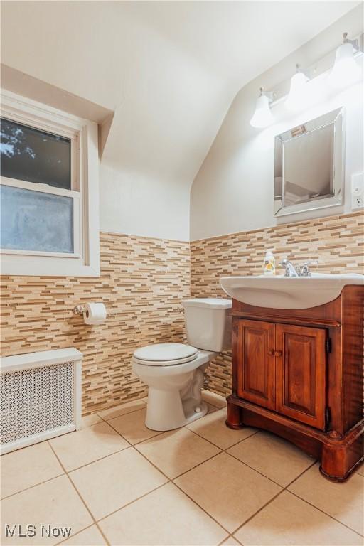 bathroom with vanity, lofted ceiling, tile patterned flooring, toilet, and tile walls