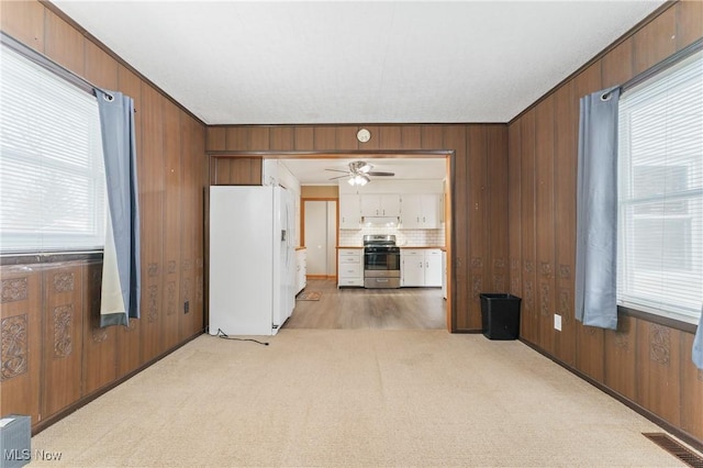 unfurnished living room with ceiling fan, crown molding, light carpet, and wooden walls