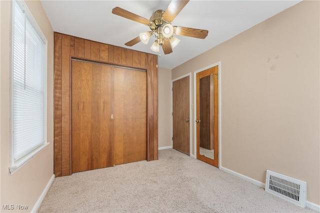 unfurnished bedroom with ceiling fan, wood walls, light colored carpet, and multiple windows