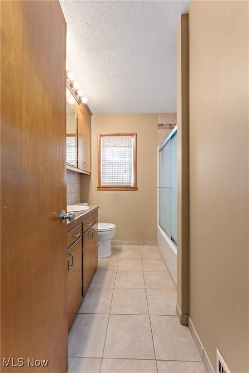 full bathroom with a textured ceiling, vanity, shower / bath combination with glass door, tile patterned flooring, and toilet