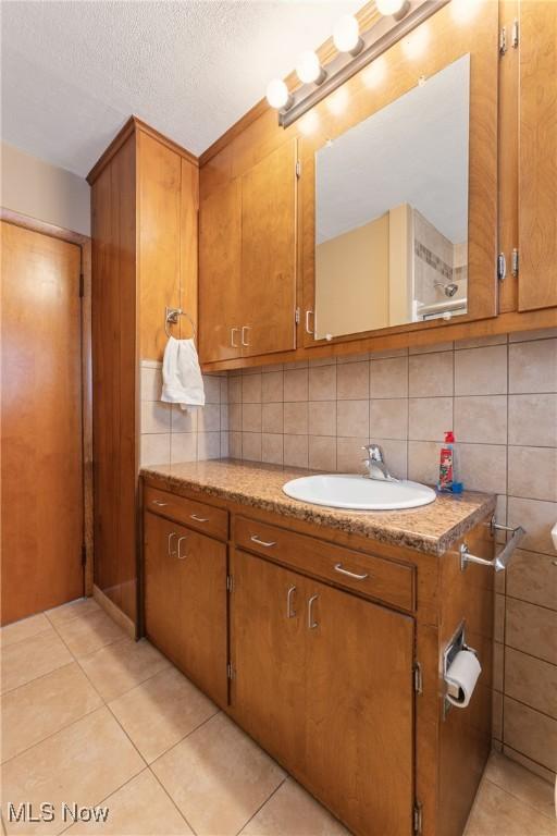 bathroom with a textured ceiling, vanity, tile patterned floors, and backsplash