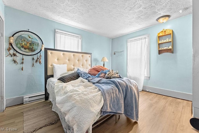 bedroom with baseboard heating, light hardwood / wood-style floors, and a textured ceiling