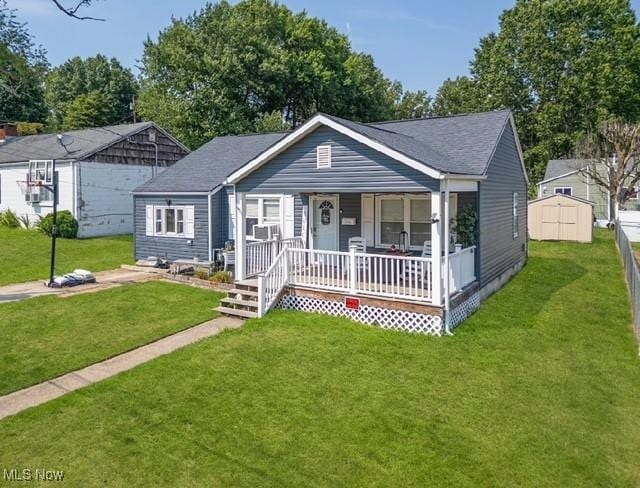 view of front of property with covered porch, a front yard, and a storage shed