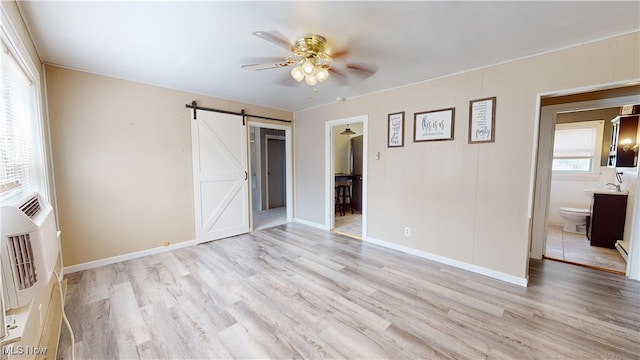 unfurnished bedroom featuring ensuite bath, ceiling fan, a barn door, light hardwood / wood-style floors, and multiple windows