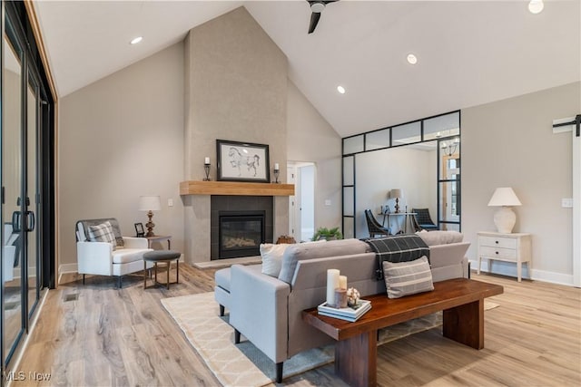 living room featuring a tile fireplace, ceiling fan, high vaulted ceiling, and light hardwood / wood-style floors