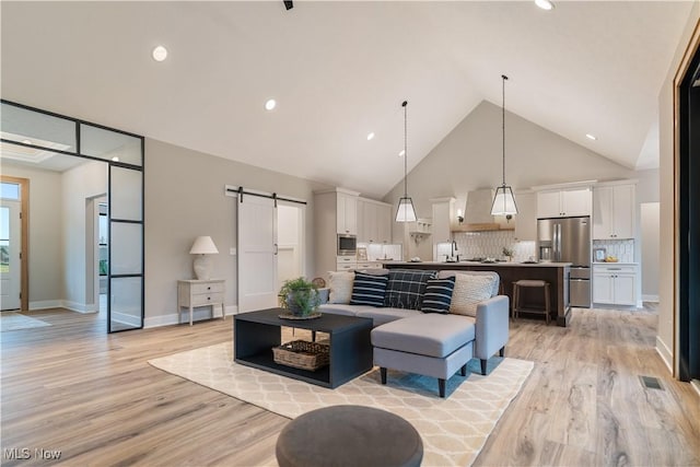 living room featuring a barn door, light hardwood / wood-style floors, and high vaulted ceiling