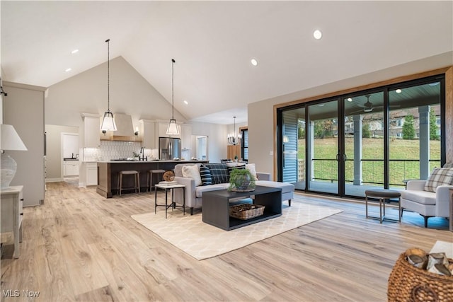 living room with a notable chandelier, light wood-type flooring, and high vaulted ceiling