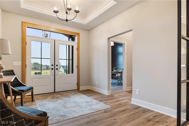 foyer featuring french doors, crown molding, light hardwood / wood-style flooring, a tray ceiling, and a chandelier