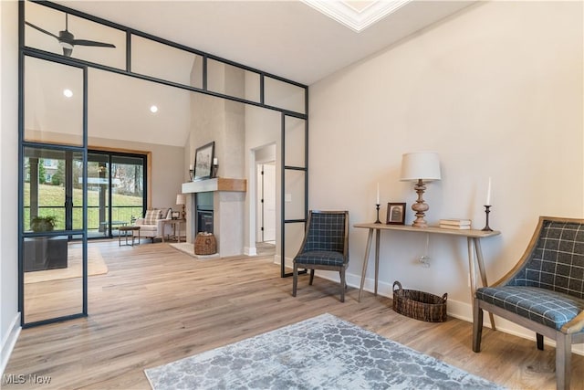 living area with wood-type flooring, a large fireplace, and ceiling fan