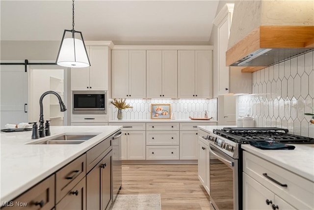 kitchen featuring sink, wall chimney range hood, a barn door, pendant lighting, and appliances with stainless steel finishes