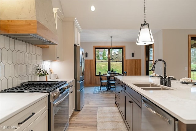 kitchen featuring sink, wall chimney exhaust hood, decorative light fixtures, white cabinetry, and stainless steel appliances