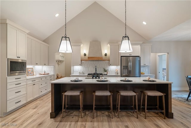 kitchen featuring stainless steel appliances, tasteful backsplash, premium range hood, a large island with sink, and a kitchen bar