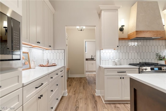 kitchen featuring stainless steel gas stove, premium range hood, white cabinetry, and tasteful backsplash