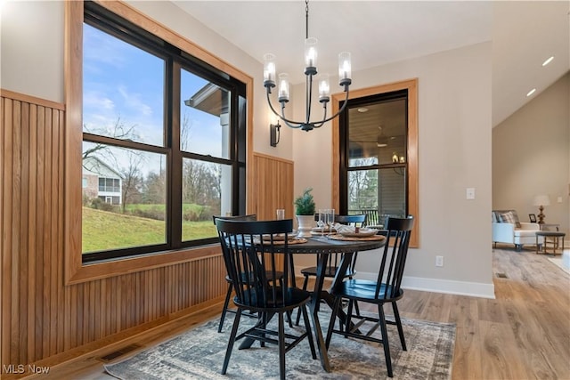 dining area with a chandelier, hardwood / wood-style flooring, a healthy amount of sunlight, and wood walls