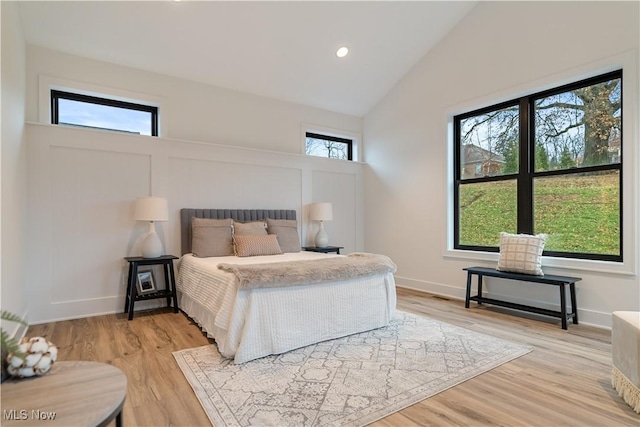 bedroom featuring multiple windows, light hardwood / wood-style floors, and lofted ceiling