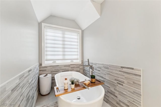 bathroom with vaulted ceiling, tile walls, and a tub