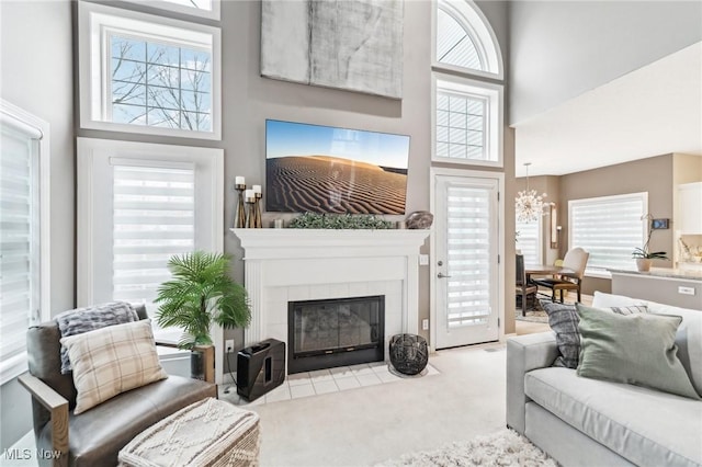 living room with a tiled fireplace, light carpet, a chandelier, and a high ceiling