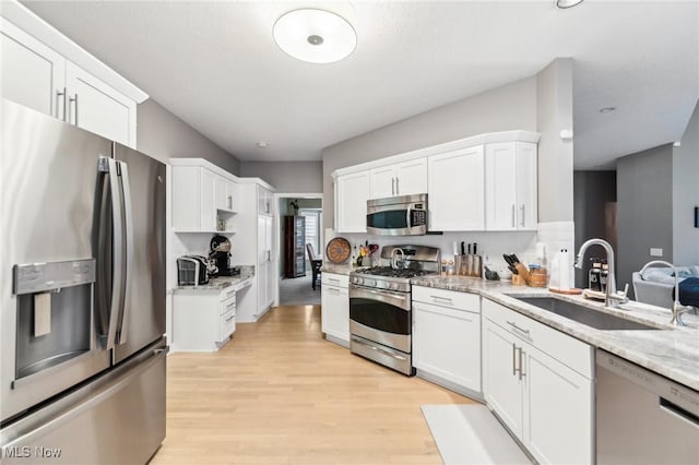 kitchen featuring light stone countertops, stainless steel appliances, white cabinetry, and sink