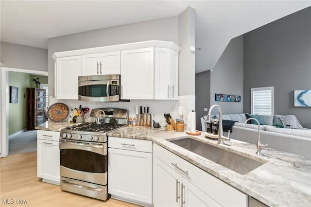 kitchen with white cabinets, sink, light stone countertops, appliances with stainless steel finishes, and light hardwood / wood-style floors