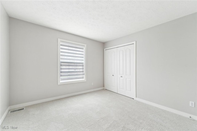 unfurnished bedroom featuring a textured ceiling, light colored carpet, and a closet