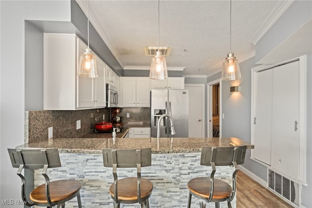 kitchen featuring kitchen peninsula, appliances with stainless steel finishes, decorative backsplash, white cabinets, and a breakfast bar area