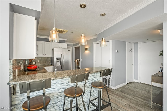 kitchen with kitchen peninsula, stainless steel fridge with ice dispenser, a textured ceiling, tasteful backsplash, and white cabinetry