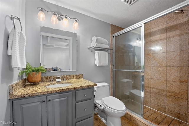 bathroom with vanity, toilet, a shower with shower door, and a textured ceiling