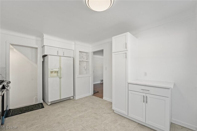 kitchen featuring white cabinetry and white refrigerator with ice dispenser