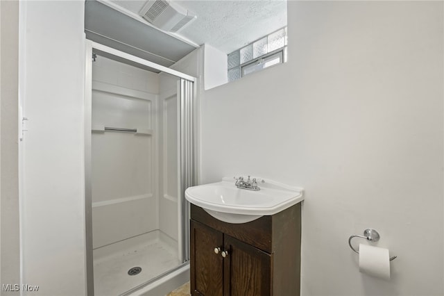 bathroom with vanity, a shower with shower door, and a textured ceiling