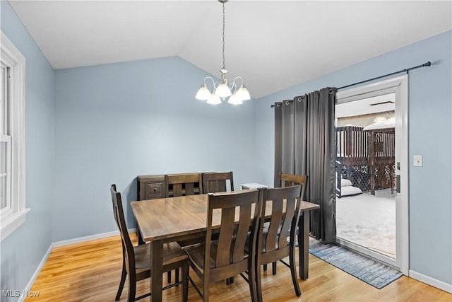 dining area featuring a notable chandelier, light wood-type flooring, and vaulted ceiling