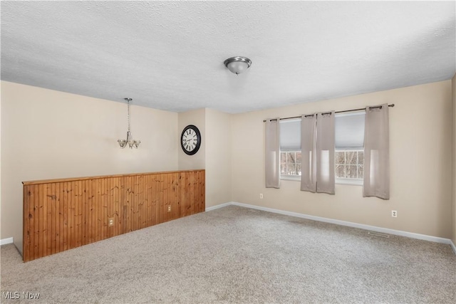 carpeted spare room featuring wooden walls, a textured ceiling, and an inviting chandelier