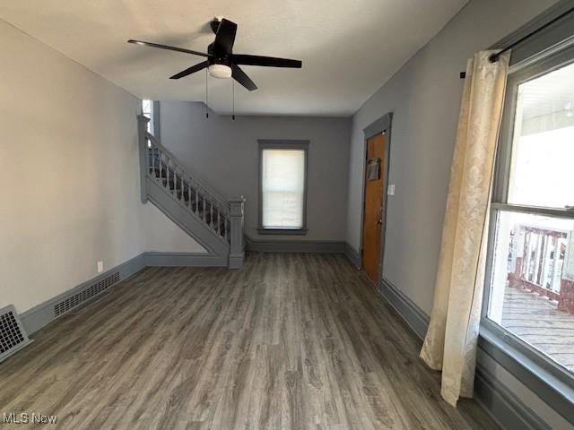 unfurnished living room with a wealth of natural light, baseboards, wood finished floors, and stairs