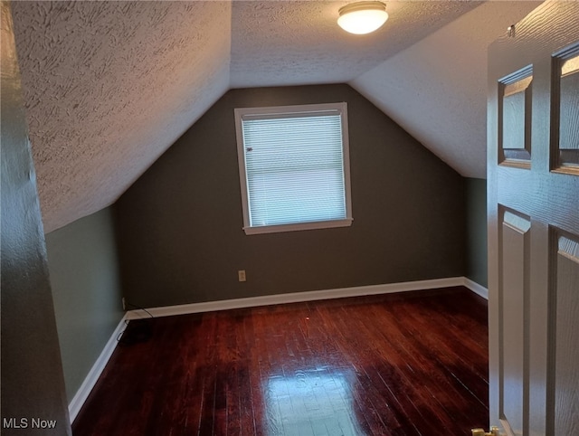 additional living space with lofted ceiling, dark hardwood / wood-style flooring, and a textured ceiling