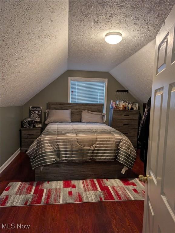 bedroom featuring lofted ceiling, dark wood-type flooring, and a textured ceiling