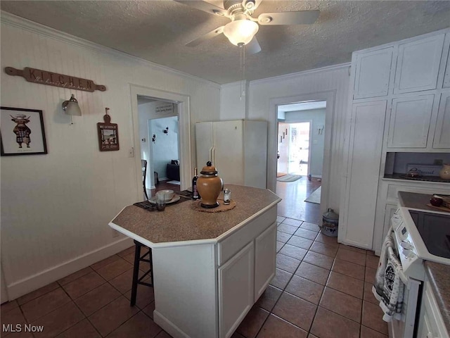 kitchen featuring crown molding, a center island, tile patterned floors, white appliances, and a ceiling fan