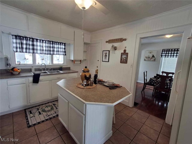 kitchen with tile patterned floors, a kitchen island, white cabinets, ornamental molding, and a sink