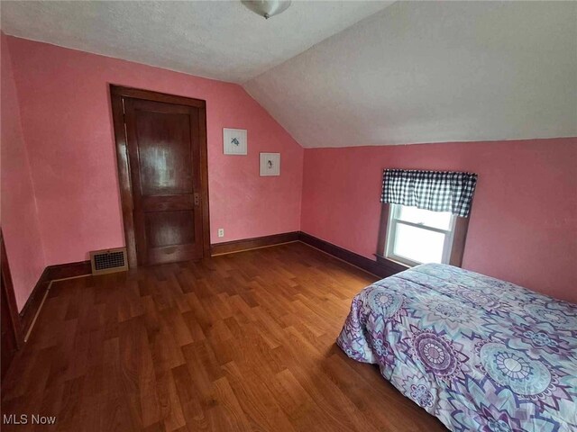 unfurnished bedroom with wood-type flooring, a textured ceiling, and vaulted ceiling