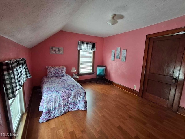 bedroom with baseboards, wood finished floors, a textured ceiling, and lofted ceiling