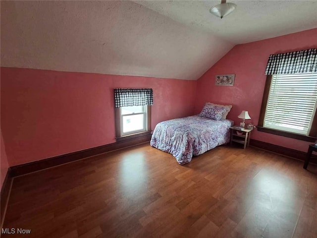 bedroom featuring a textured ceiling, wood finished floors, vaulted ceiling, and multiple windows