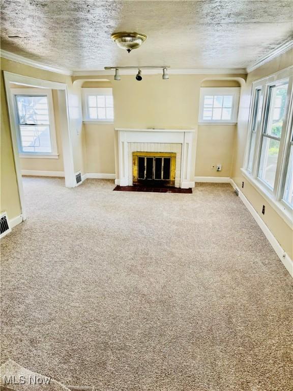 unfurnished living room with carpet flooring, rail lighting, ornamental molding, and a tile fireplace