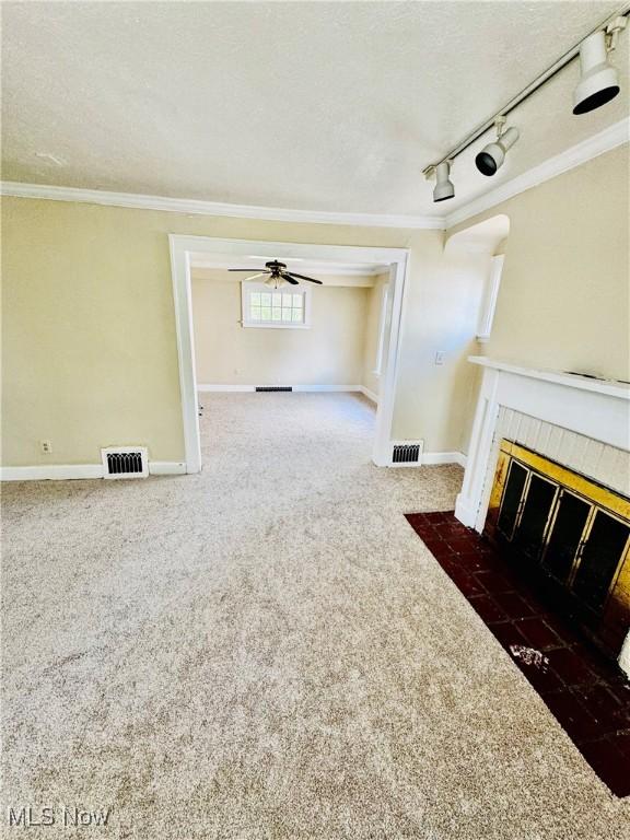 unfurnished living room with ceiling fan, a tiled fireplace, ornamental molding, dark carpet, and rail lighting