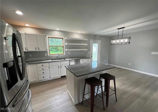 kitchen featuring white cabinetry, a center island, stainless steel appliances, decorative light fixtures, and a kitchen bar