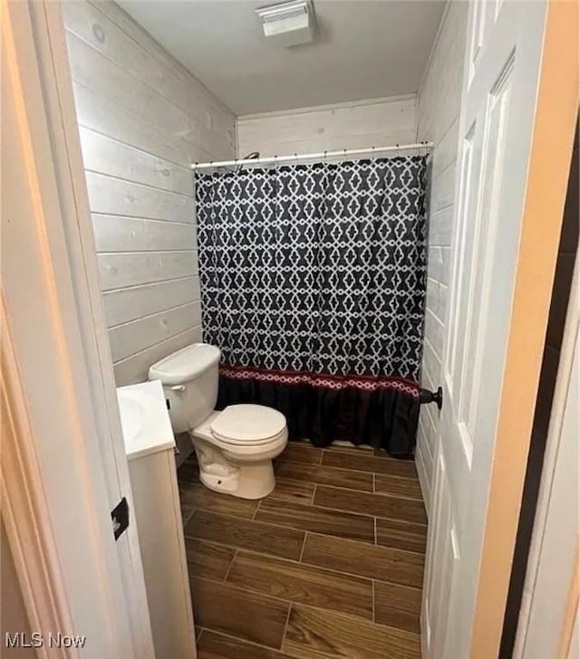 bathroom with walk in shower, wood walls, vanity, and toilet