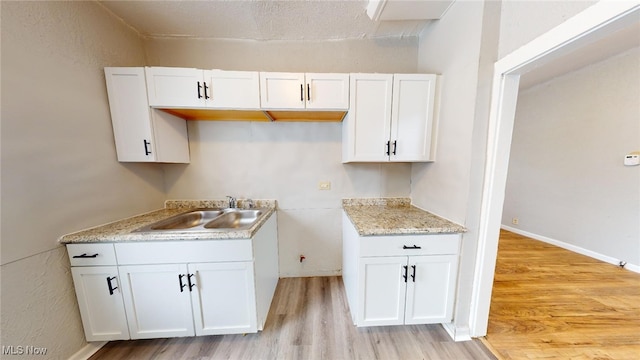 kitchen with white cabinetry, sink, and light hardwood / wood-style flooring